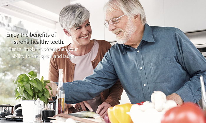 An elderly couple happily cooks together in a bright kitchen, surrounded by fresh vegetables. Text highlights benefits of dental implants for healthy teeth